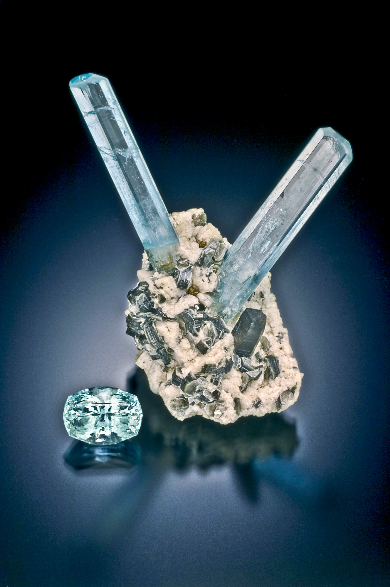 Real Mount Antero aquamarine crystals on feldspar, mica, and smoky quartz matrix beside a faceted aquamarine